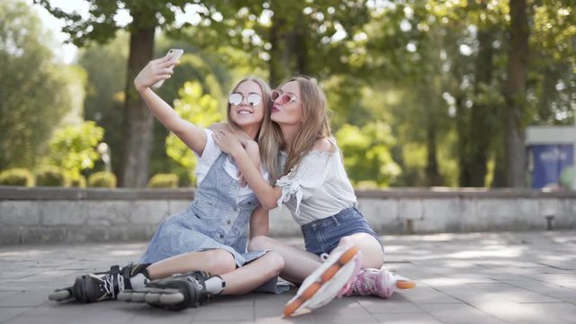 Two pretty Caucasian girls taking selfies and posing in roller-skates for social media
