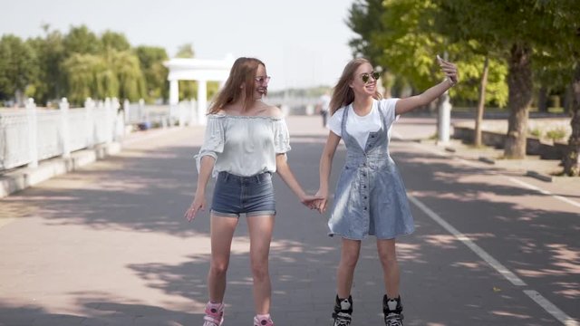 Two attractive Caucasian girls skating together holding hands and taking photos