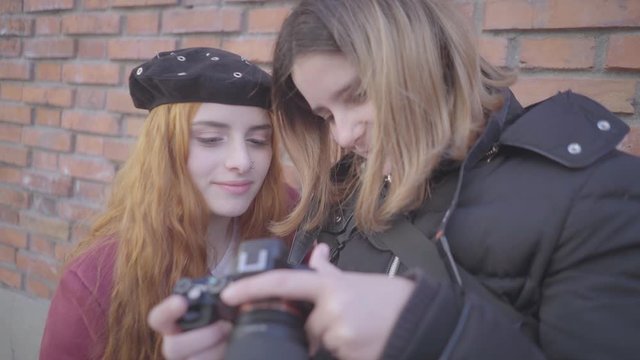 Two friends have fun taking pictures in the street. The photographer and model checking one of the photos and they smile with the result.