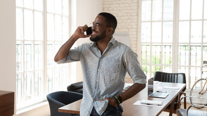 Happy african businessman standing in modern office talking on phone