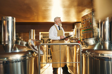 Male brewer keeping folder and controlling beer production - Powered by Adobe