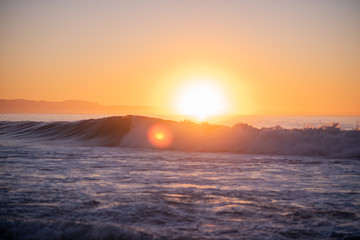 Landscape shot of waves crashing with bright sun rising over the horizon in background