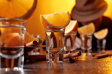 Glasses of gold tequila with orange and cinnamon sticks on a table in bar.