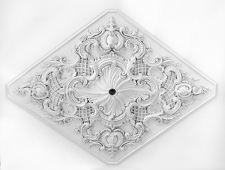 Decorative item made of white plaster on ceiling and wall. Beautiful ornament and relief stucco interior