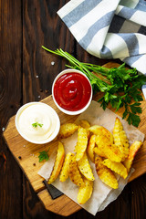 Homemade Tasty french fries on cutting board with Mayonnaise and with ketchup, on wooden table background. Top view.