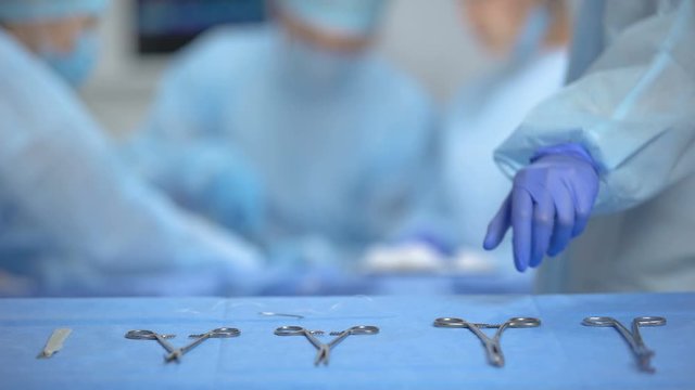 Hands of surgeon assistant taking sterile medical equipment from table, clinic