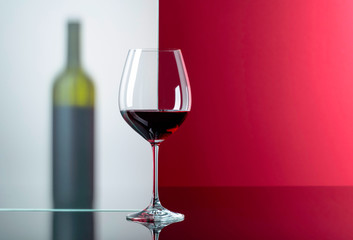 Bottle and glass of red wine on a black reflective background.