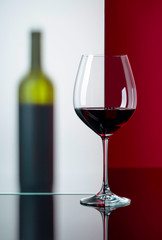 Bottle and glass of red wine on a black reflective background.