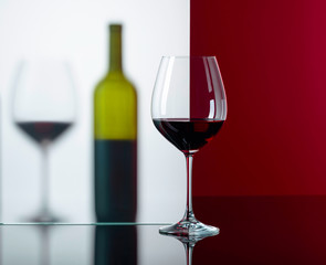 Bottle and glasses of red wine on a black reflective background.