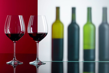 Bottles and glasses of red wine on a black reflective background.