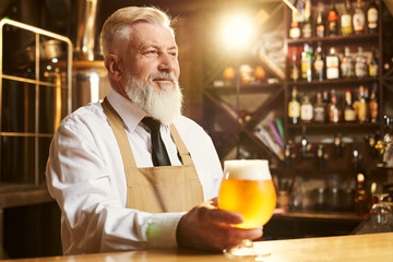 Brewer standing over bar and keeping glass of golden beer