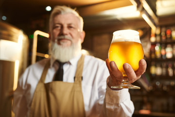 Selective focus of glass of light beer in hands of elder man