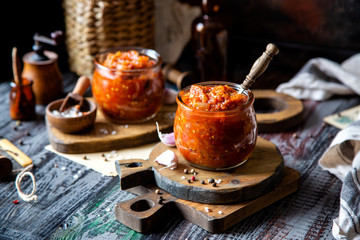 Fototapeta na wymiar two glass jars with home made red vegetable caviar, ratatouille, ragout on wooden brown boards