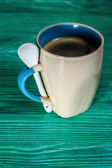 Ceramic cup on a wooden background, a teaspoon is leaning against it.