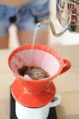 Girl barista brews coffee drip method. Pouring water from gooseneck kettle into red hario v60 funnel.
