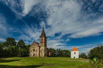 Fototapeta na wymiar Krasikov, Kokasice / Czech Republic - August 9 2019: View of the church of Mary Magdalene and a bell tower. Sunny summer day. Green grass, blue sky with white clouds.