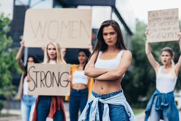 serious feminist standing with arms closed near women holding placards with feminist slogans on...