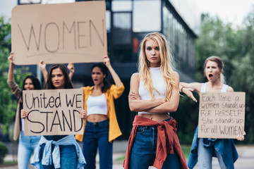 serious woman standing with arms crossed near women holding placards with feminist slogans on street