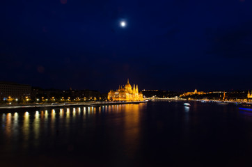 Fototapeta premium Nightscape city view of Budapest parliament under the moon lit cloudy sky and water reflection