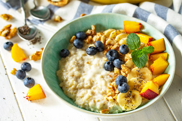 Healthy food for Breakfast, vegetarian, vegan, alkiline diet food concept. Oatmeal porridge with chia, banana and blueberry on fruits and nuts on a white wooden table.
