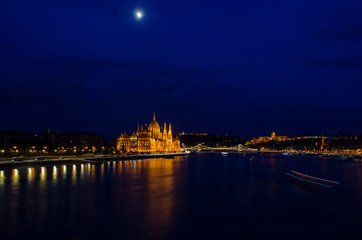 Nightscape city view of Budapest parliament under the cloud covered moon in the sky and water reflection