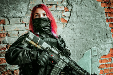 Airsoft red-hair woman in uniform with machine gun. Closeup soldier inside broken building beside...