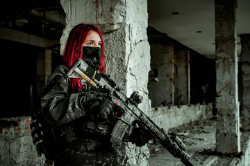 Airsoft red-head woman in uniform and put down machine gun. Close up soldier standing on balkony. Horizontal photo side view