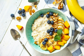Healthy food for Breakfast, vegetarian, vegan, alkiline diet food concept. Oatmeal porridge with chia, banana and blueberry on fruits and nuts on a white wooden table. Top view flat lay.
