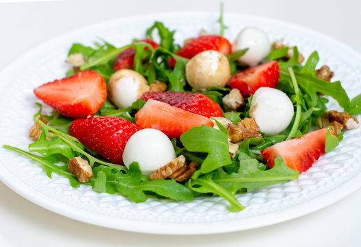 Salad with mozzarella cheese, arugula and strawberries on a white plate. Healthy summer green salad for diet, snack or light dinner.