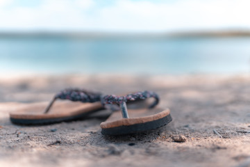 Pair of slippers on the sand at the beach while a blurry background.