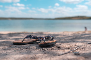 Pair of slippers on the sand at the beach while a blurry background.