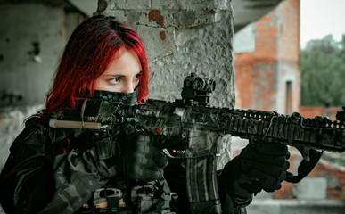 Airsoft red-head woman in uniform with machine gun standing on balkony. Close up soldier aim at the...