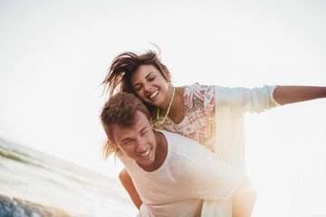 Young couple enjoying summer holidays. Handsome young man giving piggyback ride to girlfriend on beach.