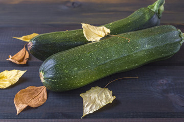 Green zucchini (squash, vegetable marrow) and autumn colorful leaves on the wooden tbackground close up.