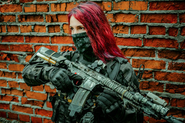 Airsoft red-hair woman in uniform with machine gun beside brick wall