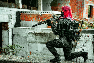 Airsoft red-hair woman in uniform with machine gun standing on knee. Soldier on ruine. side view