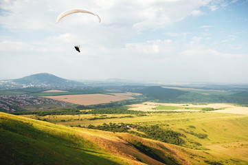 A paraglider flies in the sky in a cocoon suit on a paraglider over the Caucasian countryside with hills and mountains. Paragliding Sport Concept