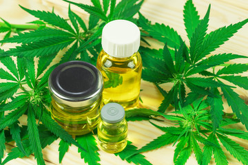 glass bottles, different shapes, with hemp oil among hemp leaves, light wooden background	