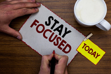 Conceptual hand writing showing Stay Focused. Business photo text Be attentive Concentrate Prioritize the task Avoid distractions Man holding marker notebook reminder wooden table cup coffee