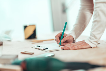 Female carpenter writing project notes in woodwork workshop