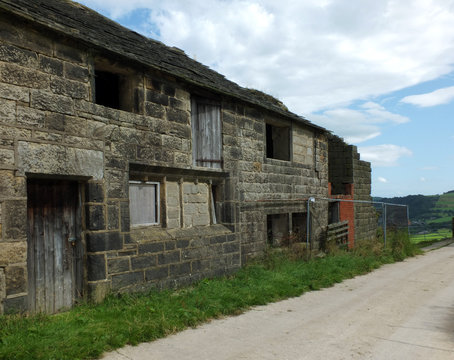 ancient abandoned stone cottage in a row of rural buildings with empty windows and wooden doors with the pavement overgrown with grass