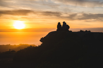 Silhouettes of friends travelers on top of a hill watching a beautiful sunset and talking, California