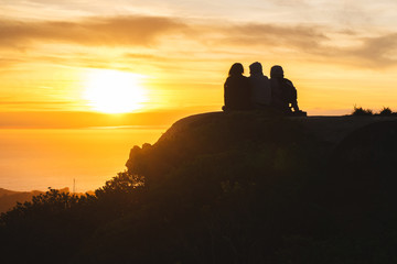 Silhouettes of friends travelers on top of a hill watching a beautiful sunset and talking, California