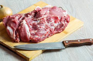 Raw meat, onion and old knife on wooden board