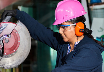 Close up of a woman who wears industrial safety equipment and is cutting metal with a miter saw