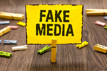 Text sign showing Fake Media. Conceptual photo An formation held by brodcasters which we cannot rely on Clothespin holding yellow paper note several clothespins wooden floor