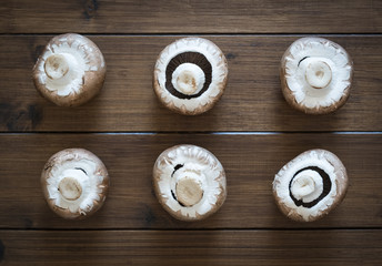 Brown champignons on the wooden background, top view