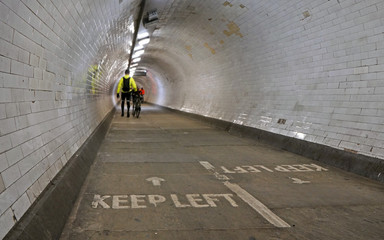 Cyclist wearing yellow jacket walking with his bicycle inside Greenwich foot tunnel under river...