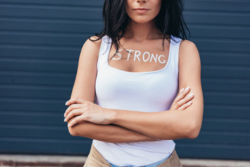cropped view of feminist with inscription strong on body standing with crossed arms