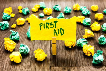 Fototapeta premium Writing note showing First Aid. Business photo showcasing Practise of healing small cuts that no need for medical training Clothespin holding yellow note paper crumpled papers several tries